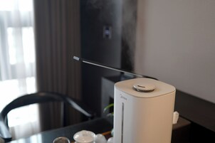 Una habitación moderna y minimalista con un purificador de aire blanco sobre una mesa de madera, una silla negra y un mueble de TV de color oscuro.