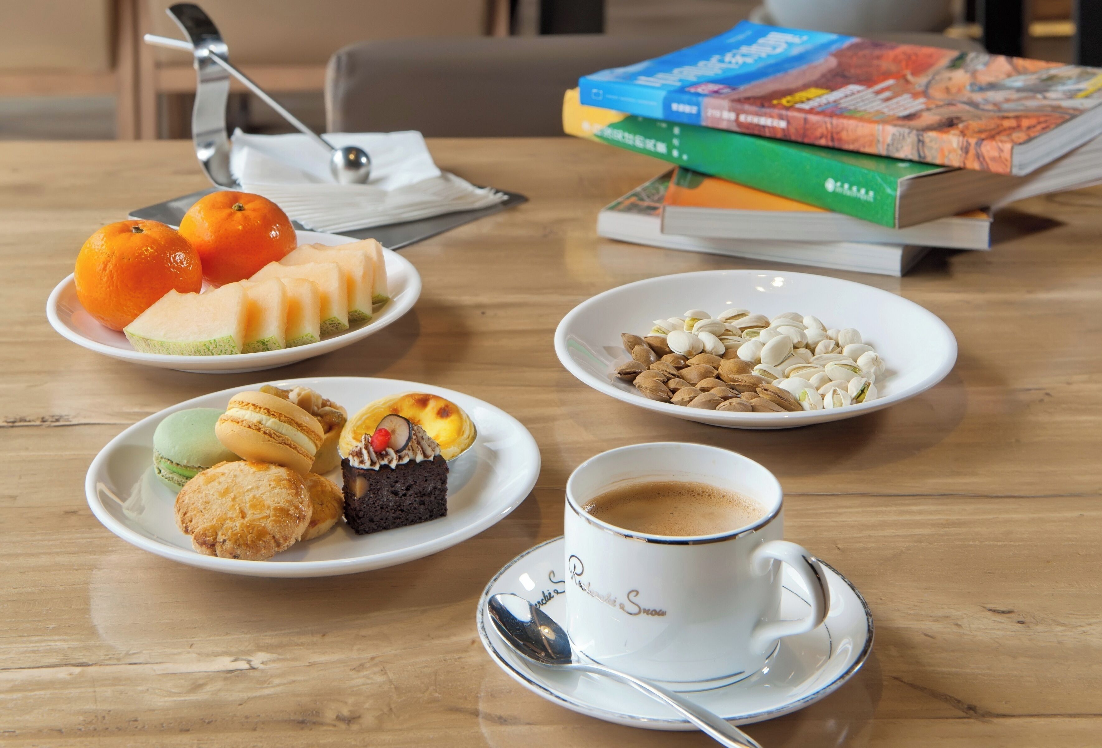 Una mesa con varios postres, una taza de café y una pila de libros.