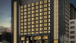 A modern hotel with a dark facade and illuminated windows, featuring a prominent entrance and vertical light strips.