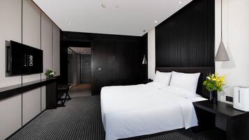 A modern hotel room with a bed, a TV, a bedside table with a lamp, and a coffee maker.