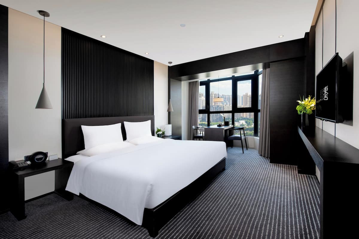 A modern hotel room with a large bed, a desk, a TV, and a city view.