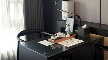 Habitación de hotel moderna con un escritorio de madera oscura, un juego de té, una planta y una lámpara.