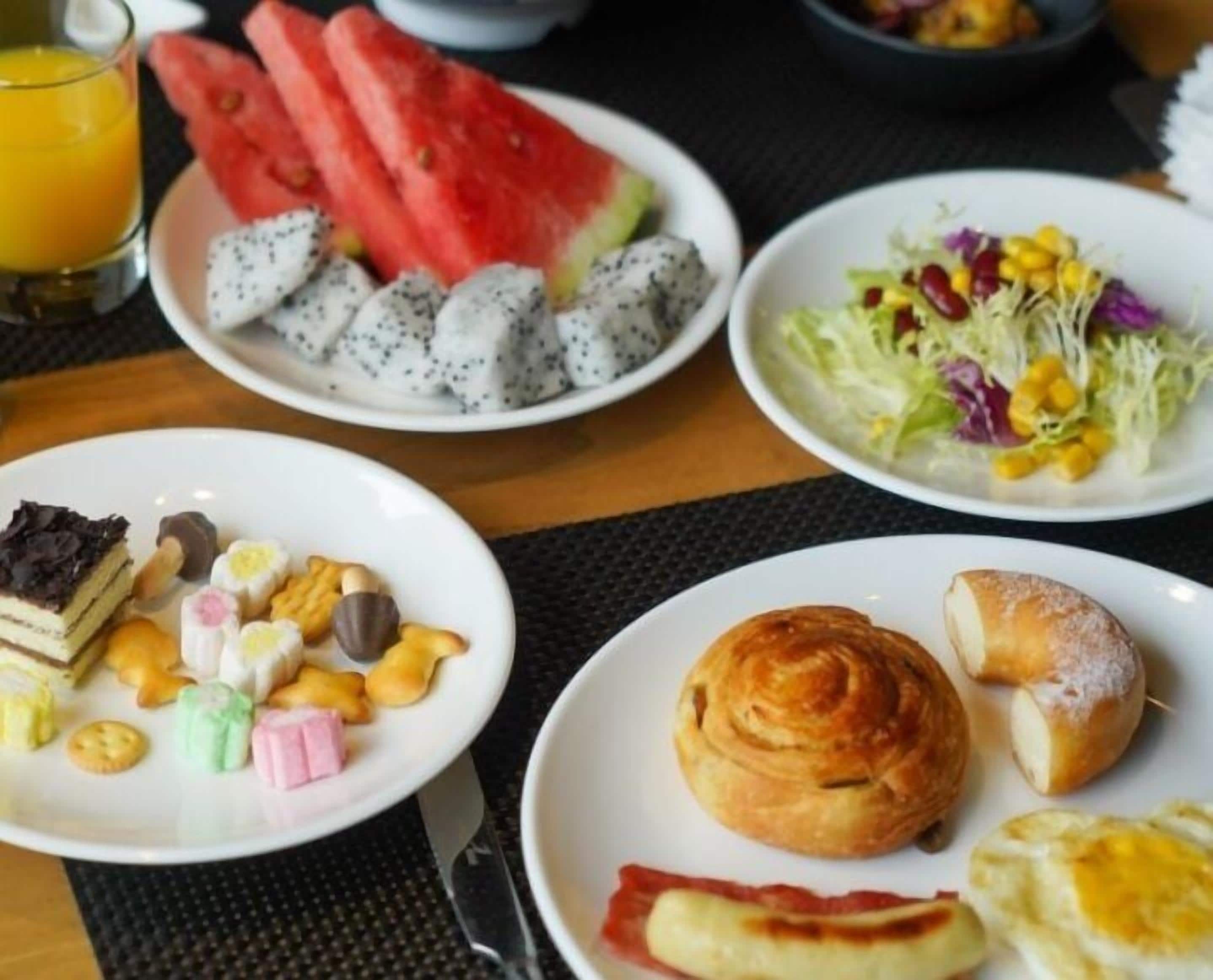 A breakfast setting with various dishes including watermelon, dragon fruit, a salad, pastries, and a drink.