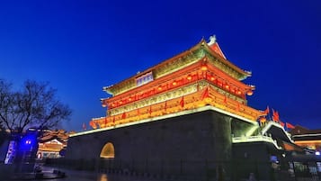 Un bâtiment traditionnel à plusieurs niveaux, agrémenté de détails rouges et dorés illuminés, doté d’une grande entrée en arc de cercle et entouré d’une cour.