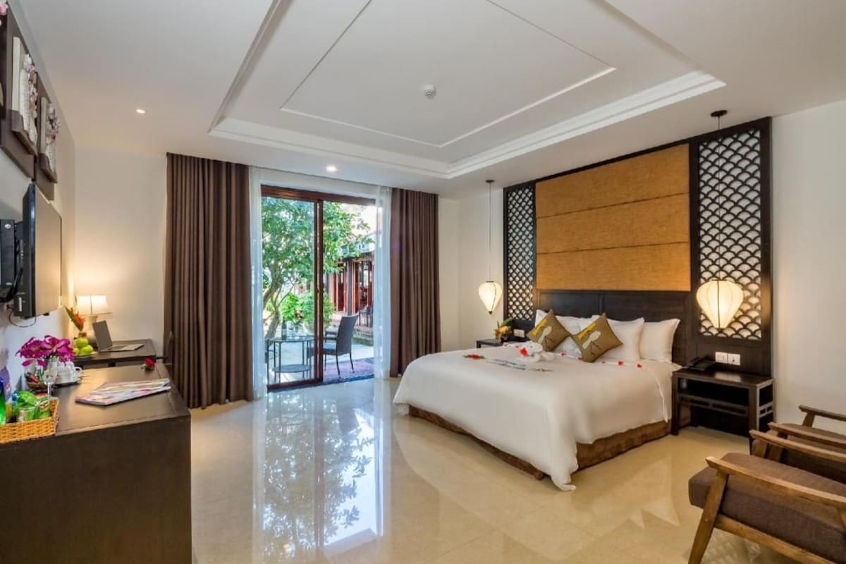 Habitación de hotel con cama, escritorio, silla, televisión y vistas al exterior.