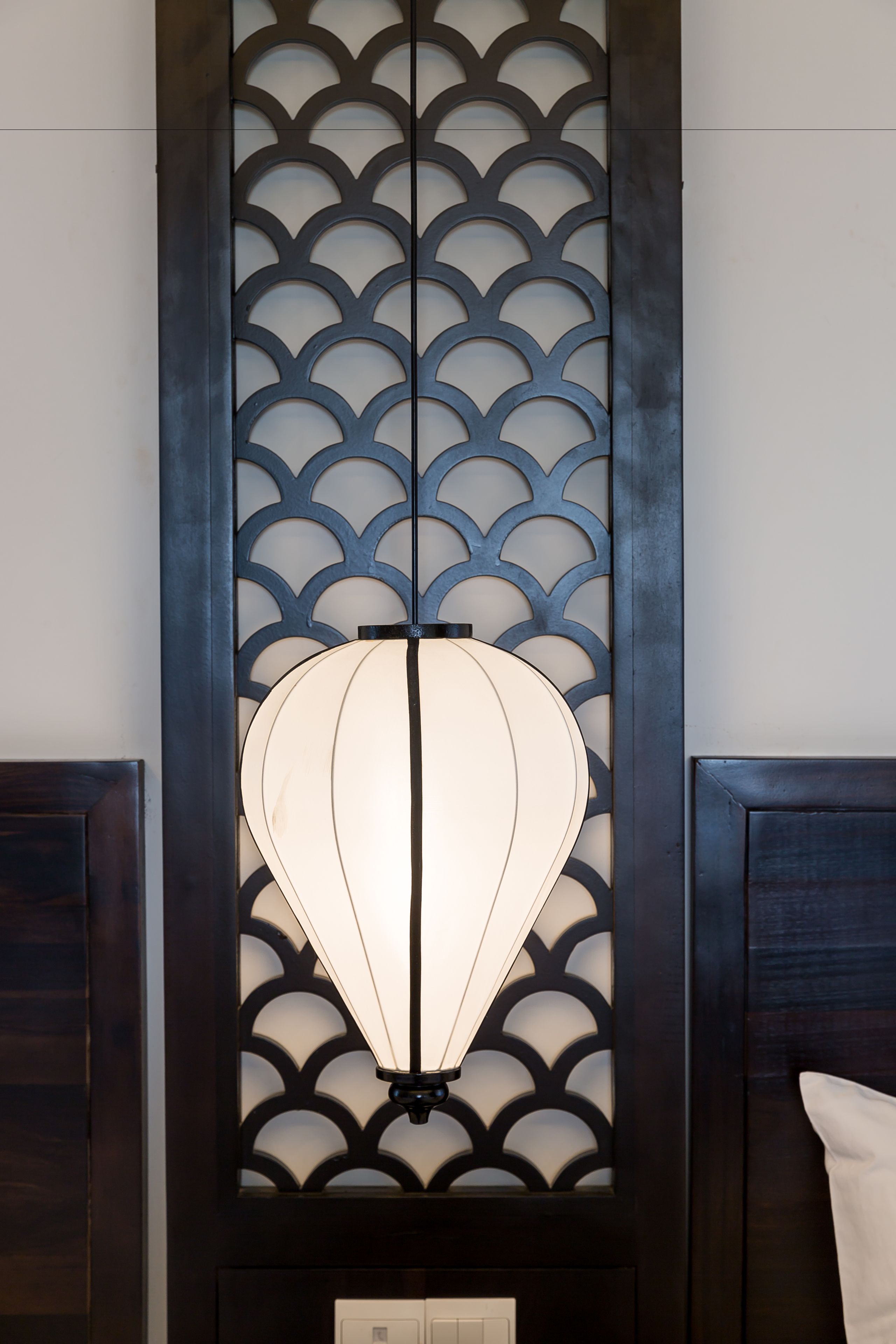 Un mur orné d’un panneau décoratif à motifs en forme de coquille, et sur lequel est suspendu un luminaire.