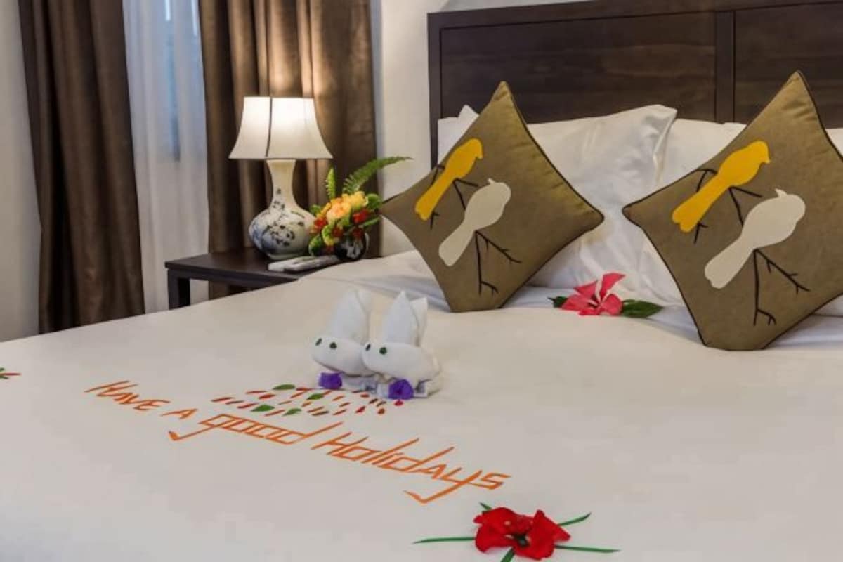 A neatly made bed with a message, pillows with bird designs, a lamp, and a vase with flowers.