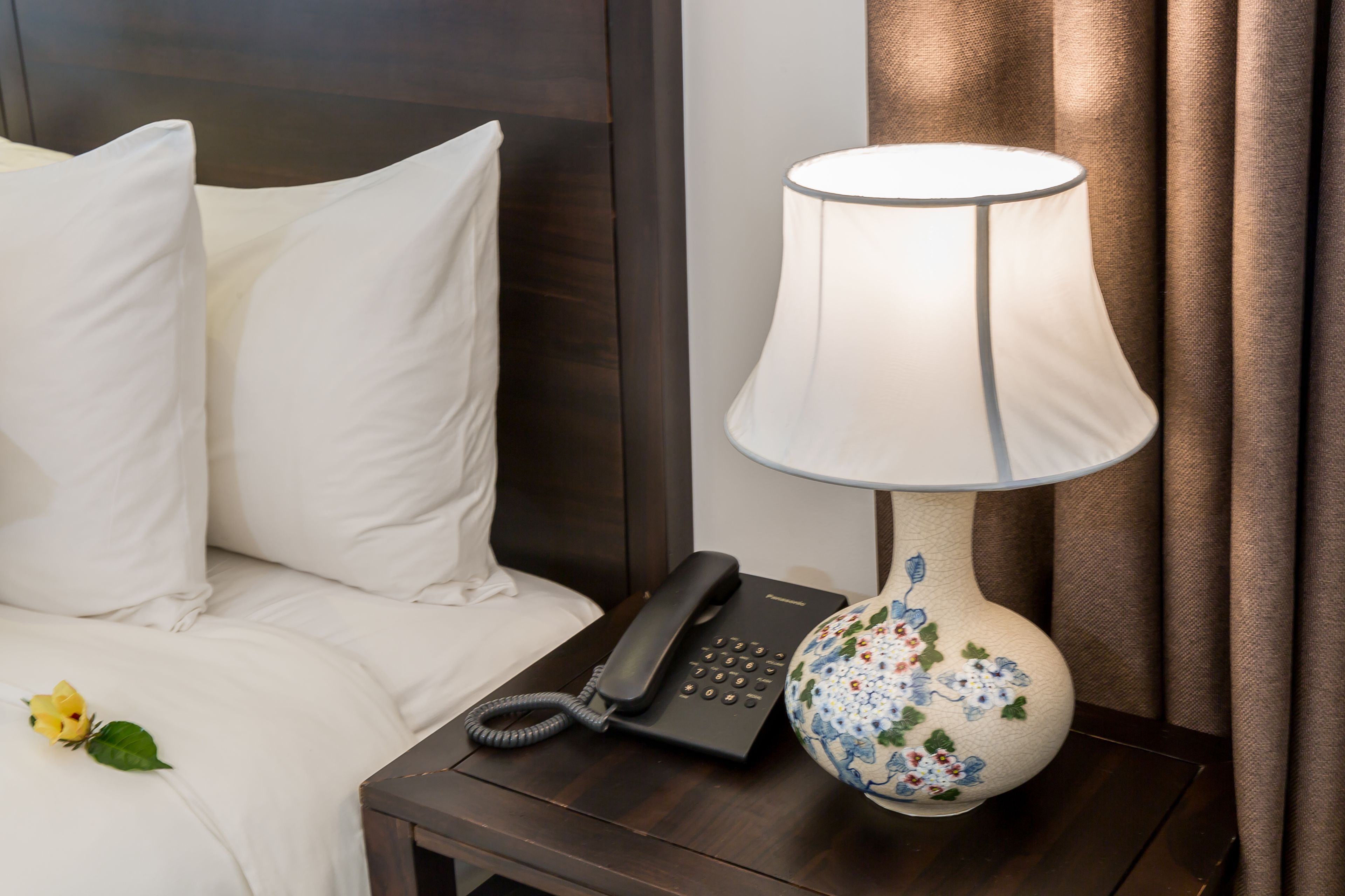 A hotel room with a bed, a bedside table with a lamp, and a telephone.