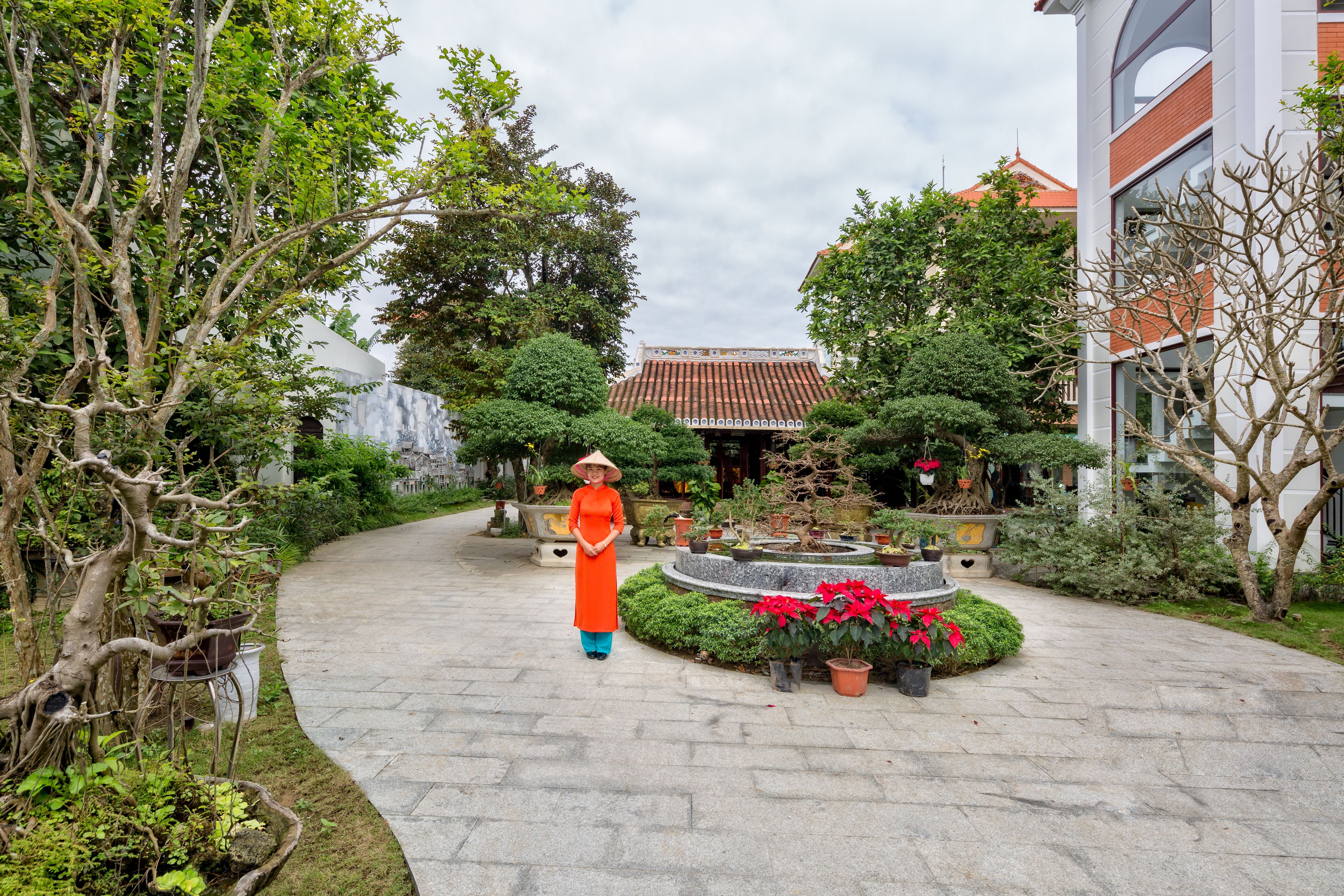 Une cour avec un chemin sinueux, des plantes en pot et, au fond, un bâtiment traditionnel doté d’un toit en tuiles.