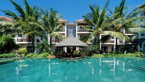 Ett semesterparadis med en kristallklar pool, palmer och en central paviljong.