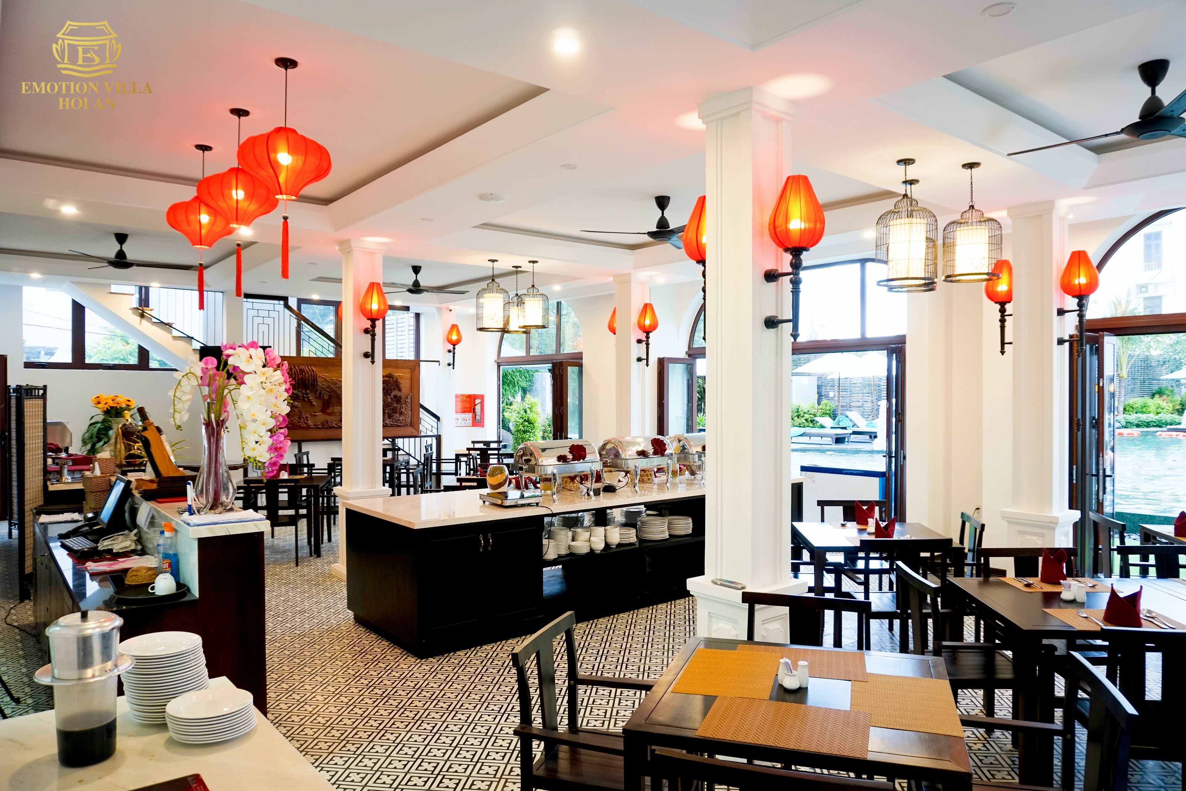 Een restaurant met een centrale bar, meerdere eettafels en rode lampionnen aan het plafond.