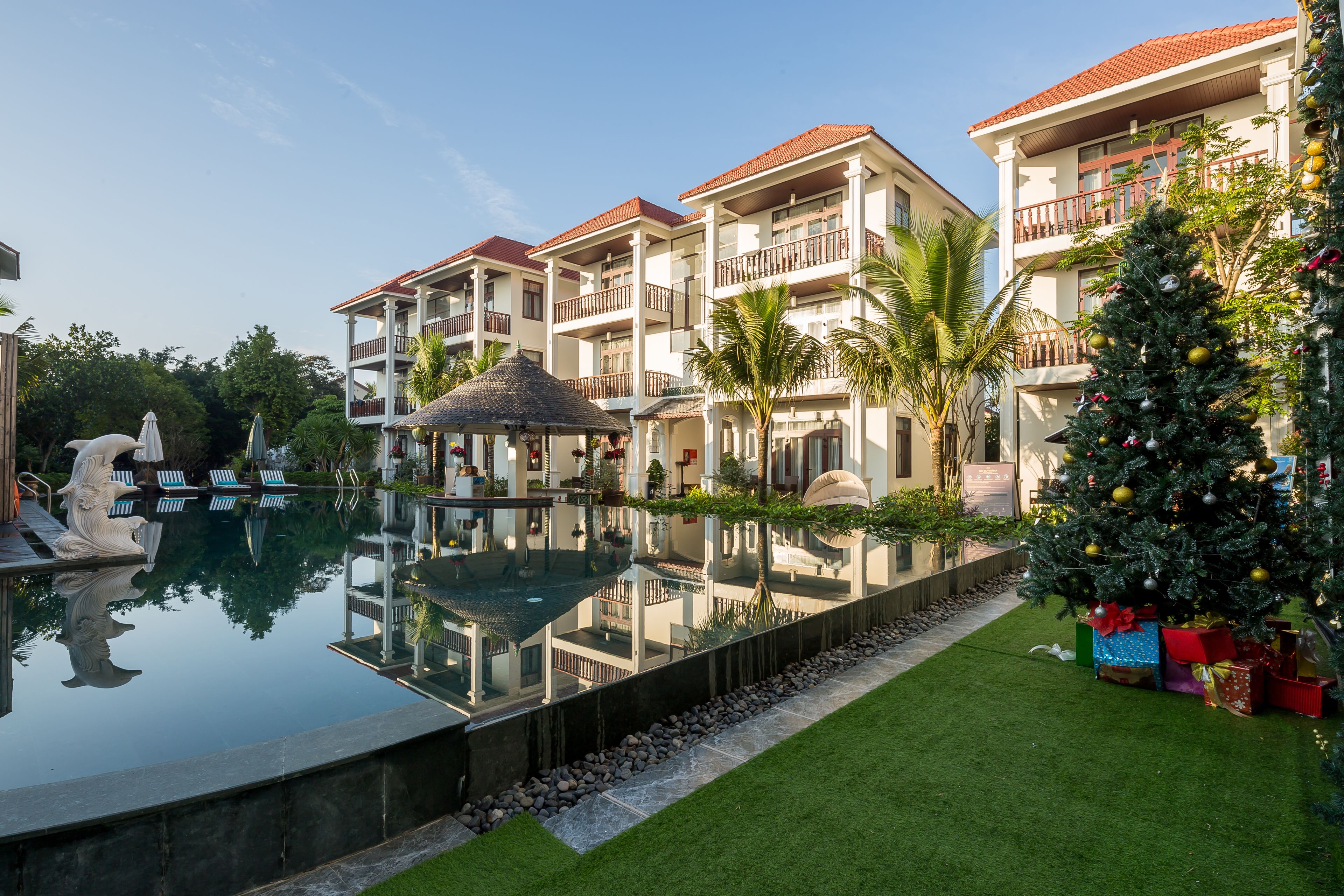 A hotel with a swimming pool, palm trees, and a Christmas tree.