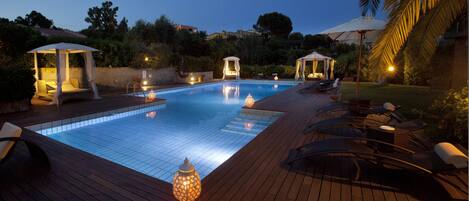 A swimming pool with lounge chairs and a gazebo, surrounded by greenery.