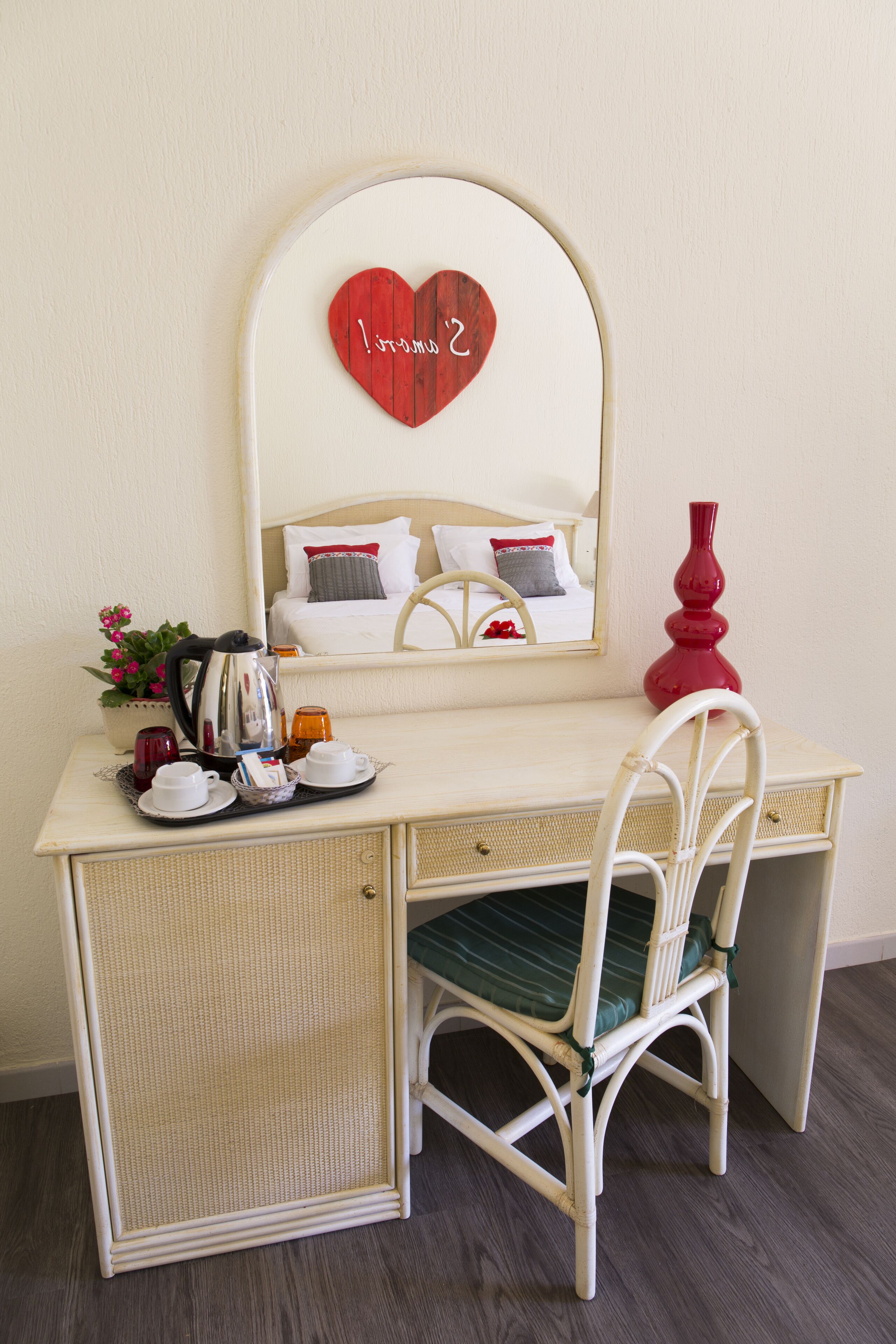 Una habitación con cama, escritorio, silla, espejo y una decoración con forma de corazón.