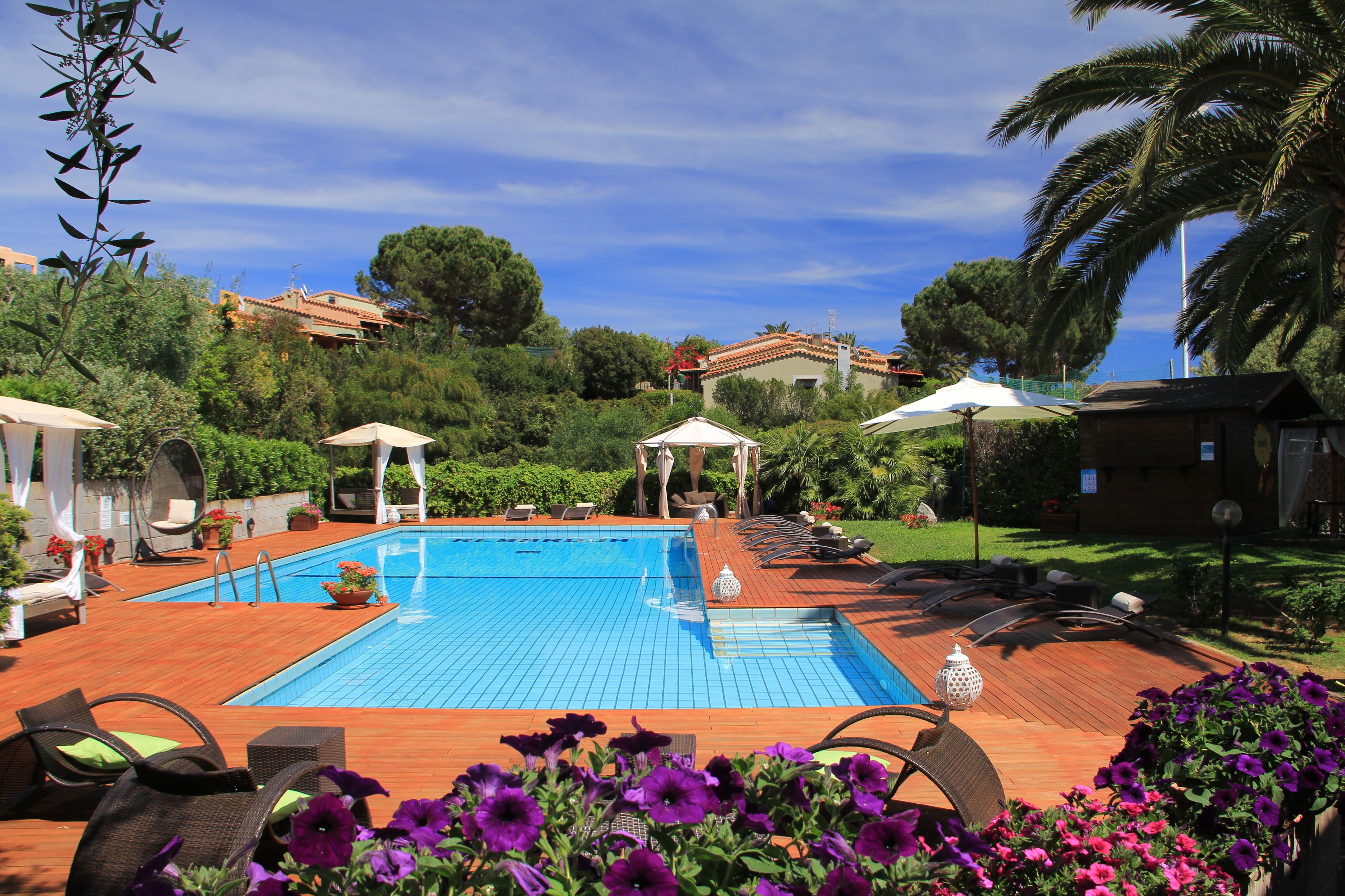 A swimming pool with lounge chairs and umbrellas, surrounded by greenery and a hill in the background.