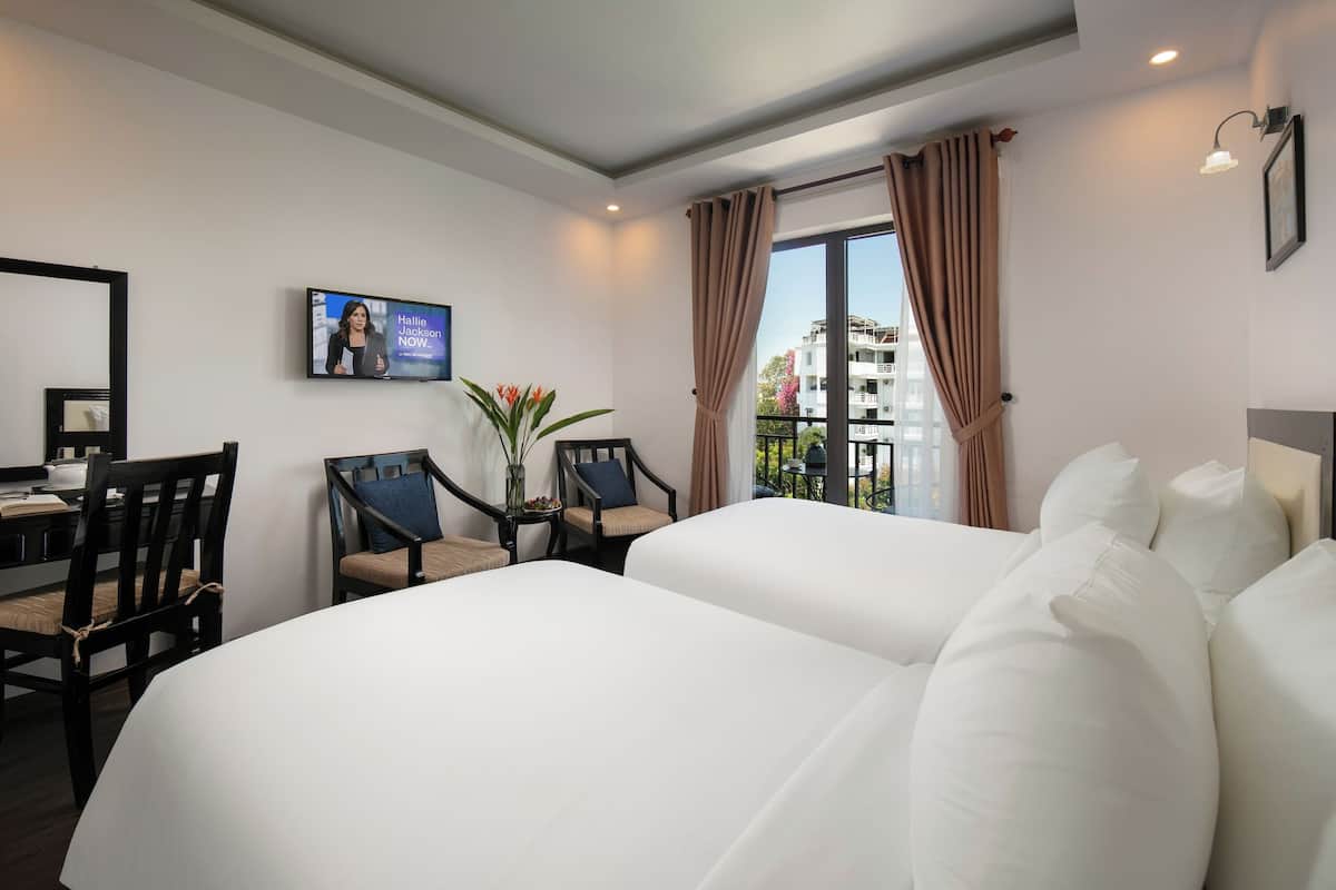 Habitación de hotel con dos camas, un escritorio con sillas, televisión y vistas al balcón.