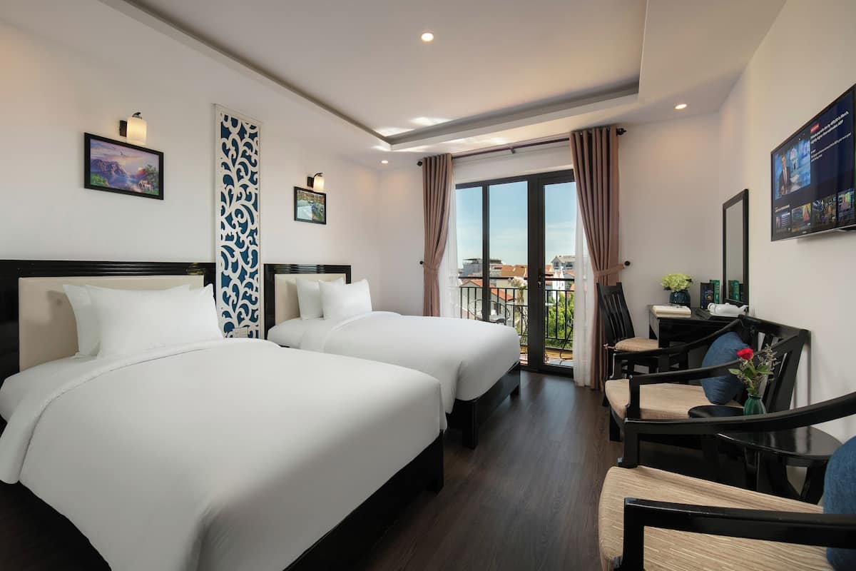 Habitación de hotel con dos camas, un escritorio con silla, televisión y balcón con vistas.