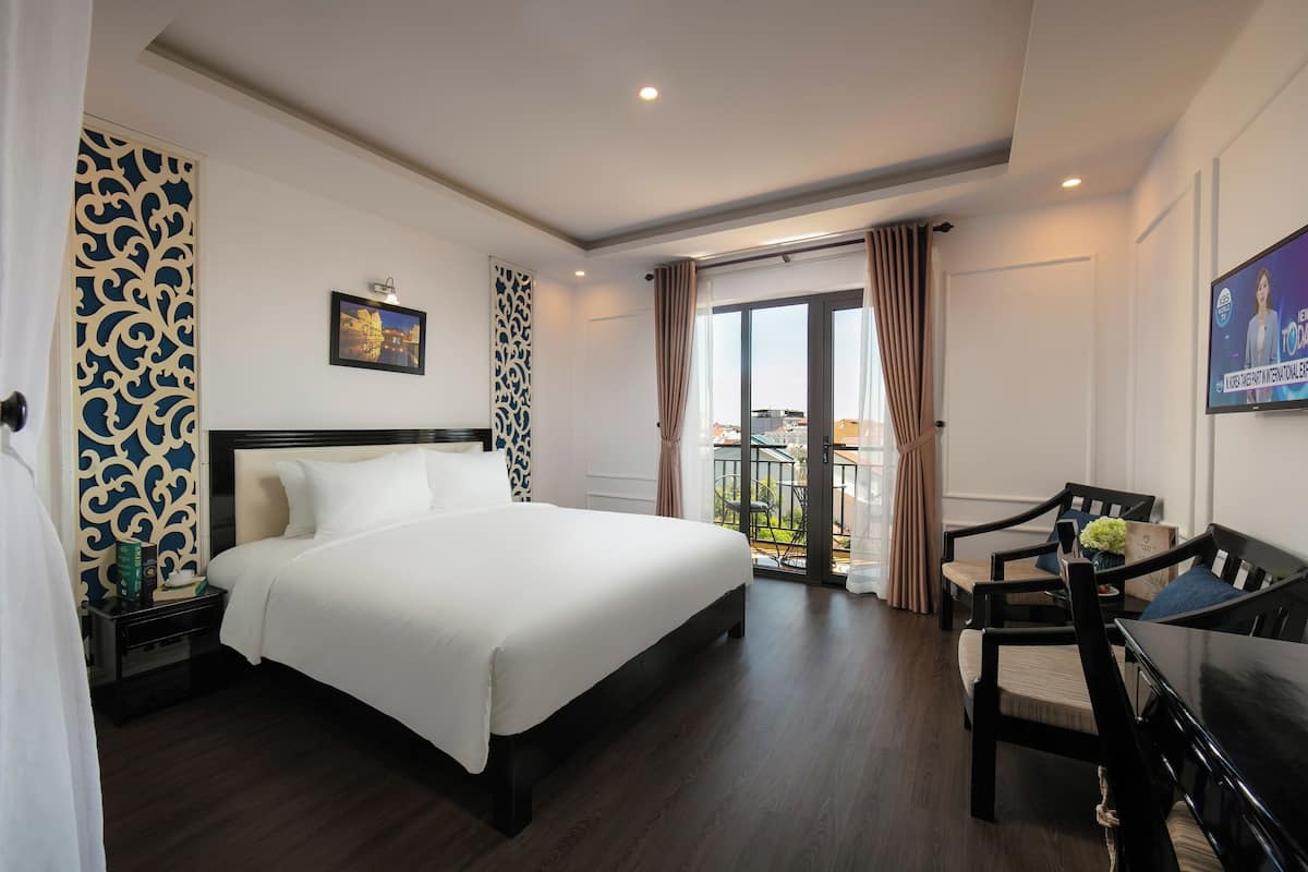 Habitación de hotel con una cama grande, un escritorio con sillas, un balcón con vistas y un televisor en la pared.