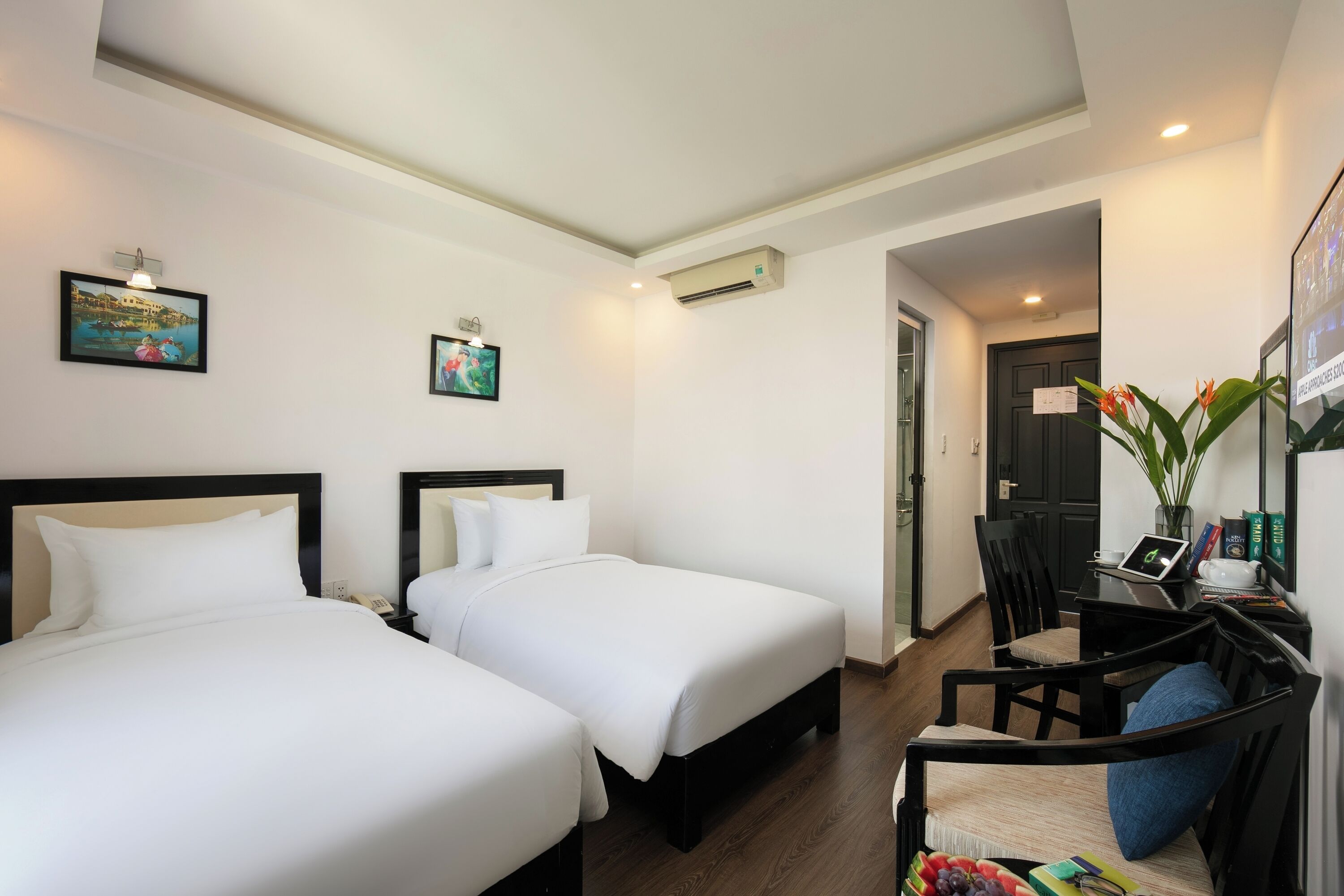 A hotel room with two beds, a desk with a laptop, a chair, and a small table with a plant.