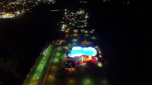 An aerial view of a resort with a large illuminated pool area, a golf course, and a well-lit beachfront.