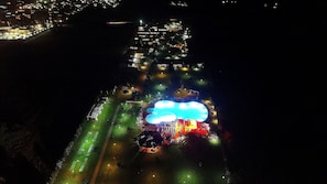 An aerial view of a resort with a large illuminated pool area, a golf course, and a well-lit beachfront. - Rey Beach Club (Muravera)