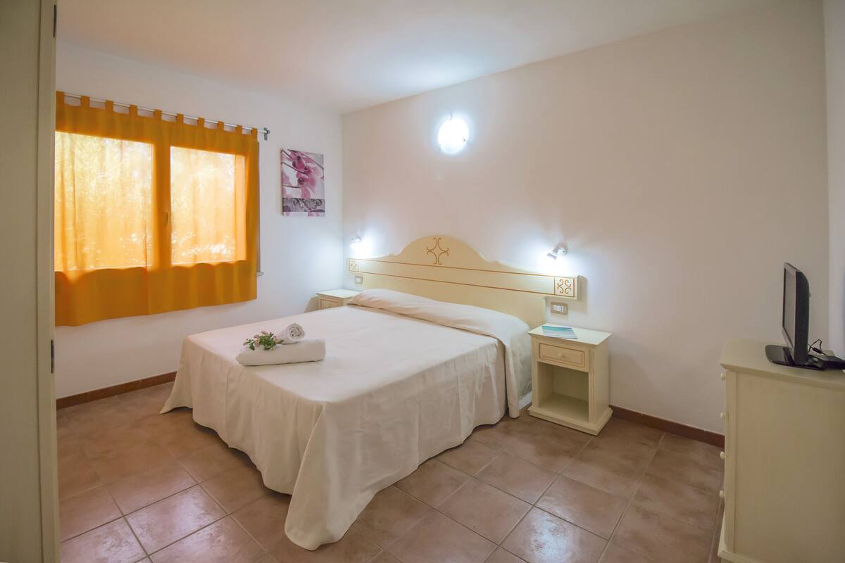 A bedroom with a bed, bedside tables, a nightstand, a TV, and a window with curtains.