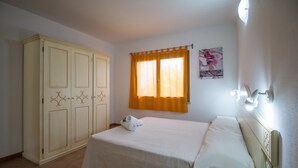 A bedroom with a bed, a wardrobe, a window with curtains, and a wall-mounted light fixture.