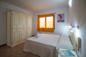A bedroom with a bed, a wardrobe, a window with curtains, and a wall-mounted light fixture.