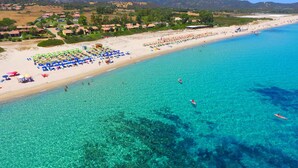 An aerial view of a beach with clear turquoise water, numerous umbrellas, and people engaging in water activities.