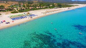 An aerial view of a beach with clear turquoise water, numerous umbrellas, and people engaging in water activities.