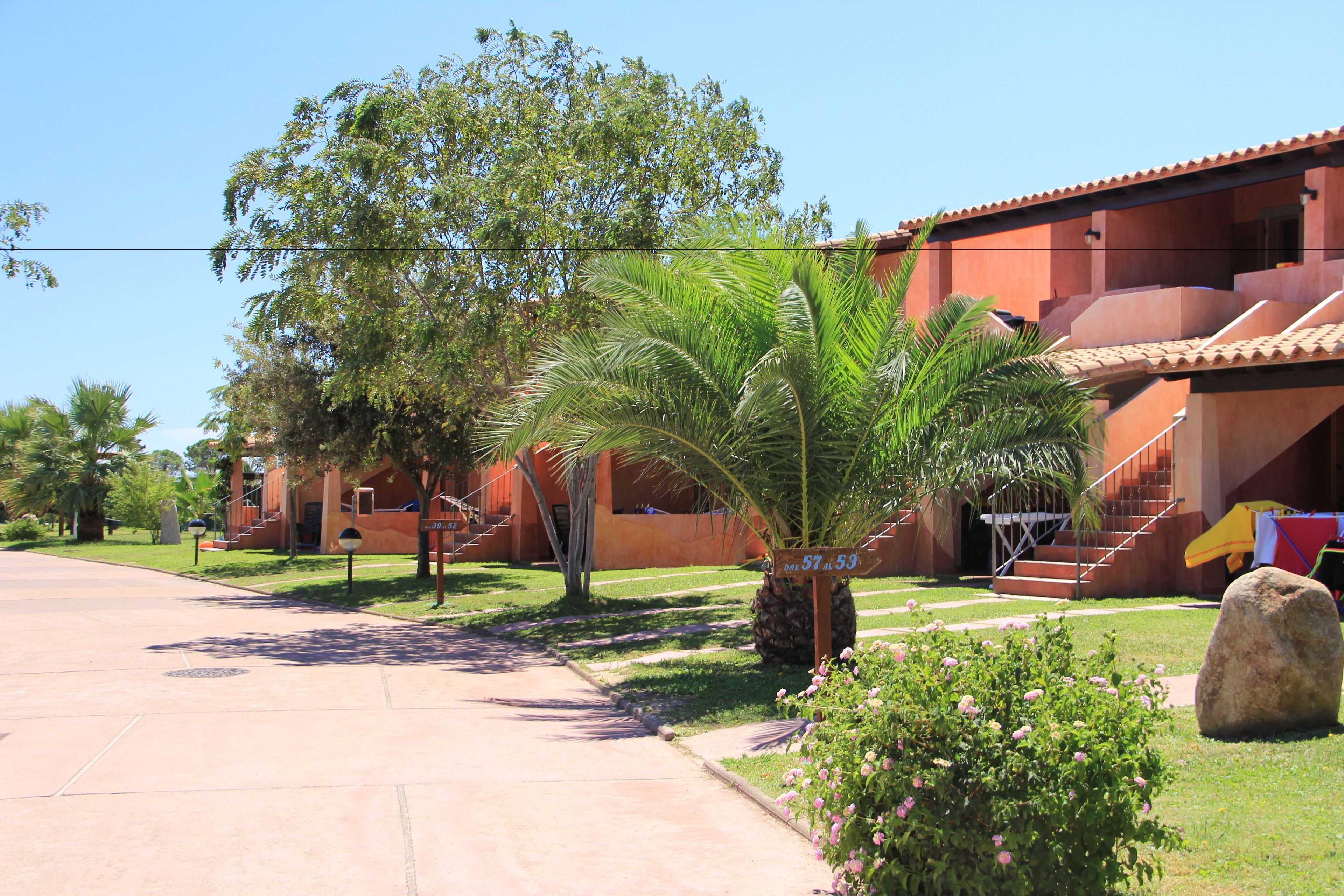 Un edificio residencial con fachada roja, una palmera y una gran roca al frente.
