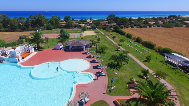An aerial view of a resort with a large swimming pool, a beach, and a golf course.