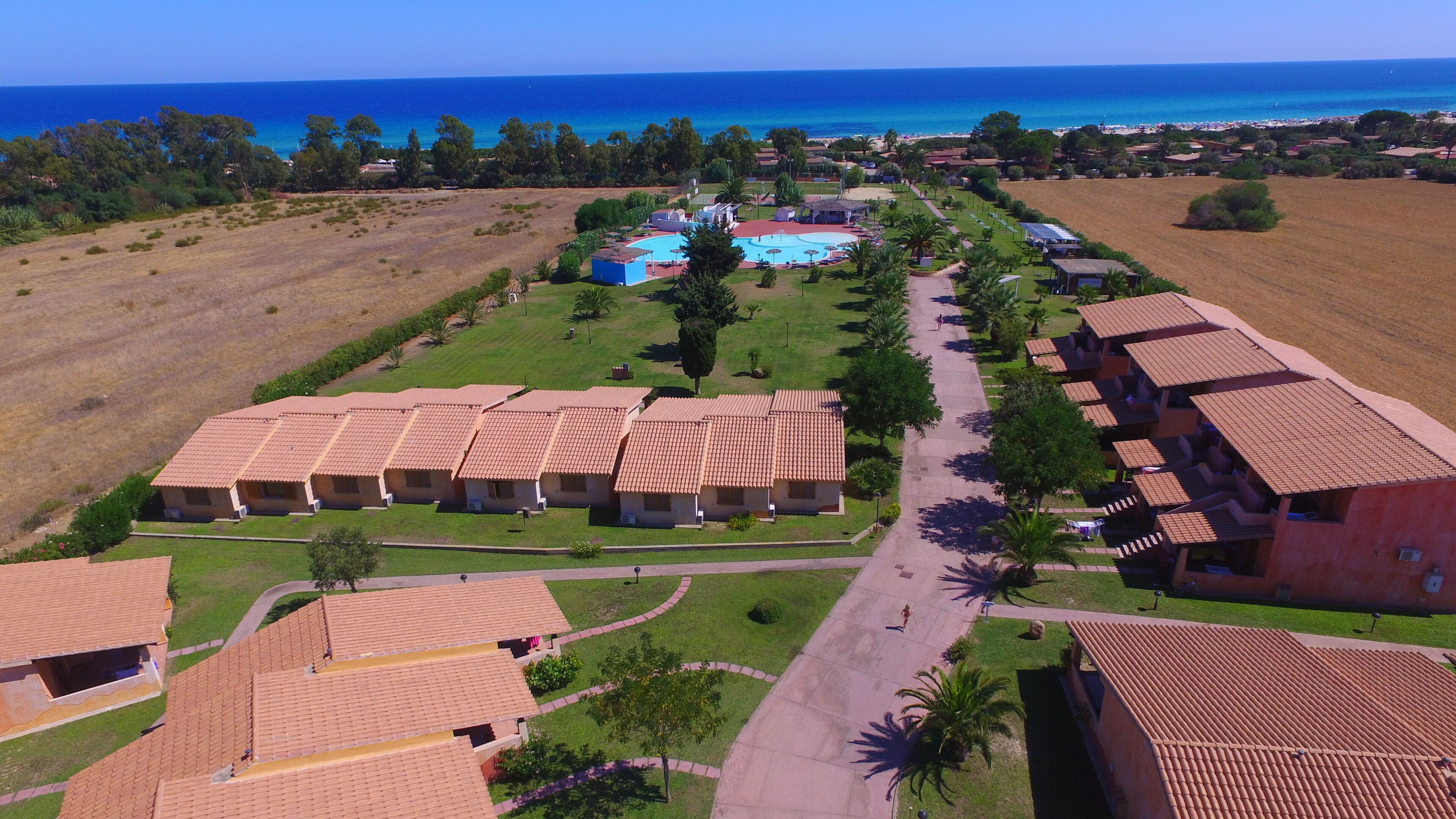 A resort with multiple bungalow-style buildings, a central swimming pool, and a view of the ocean.