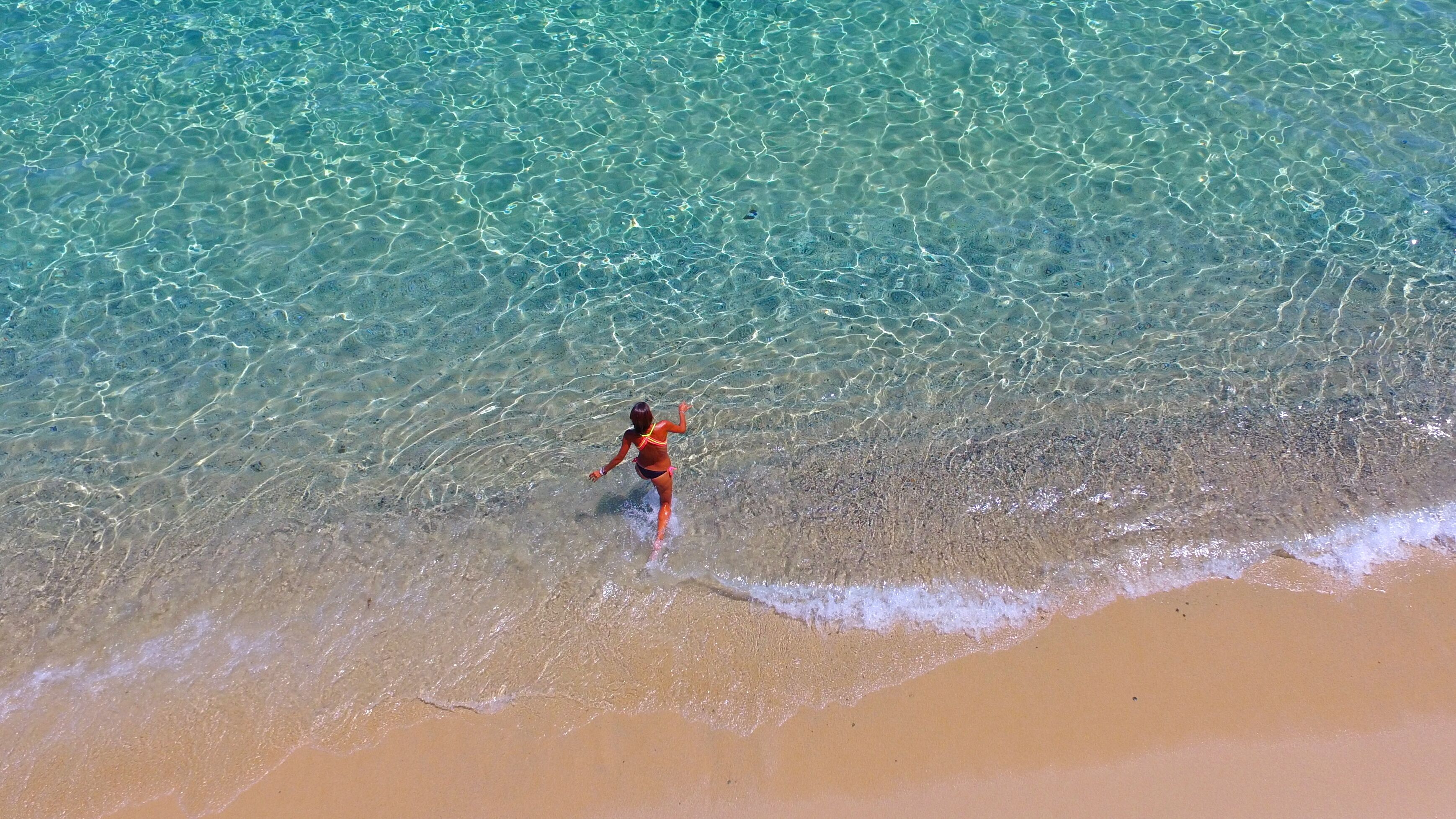 A beach scene with clear water and a person in the water.