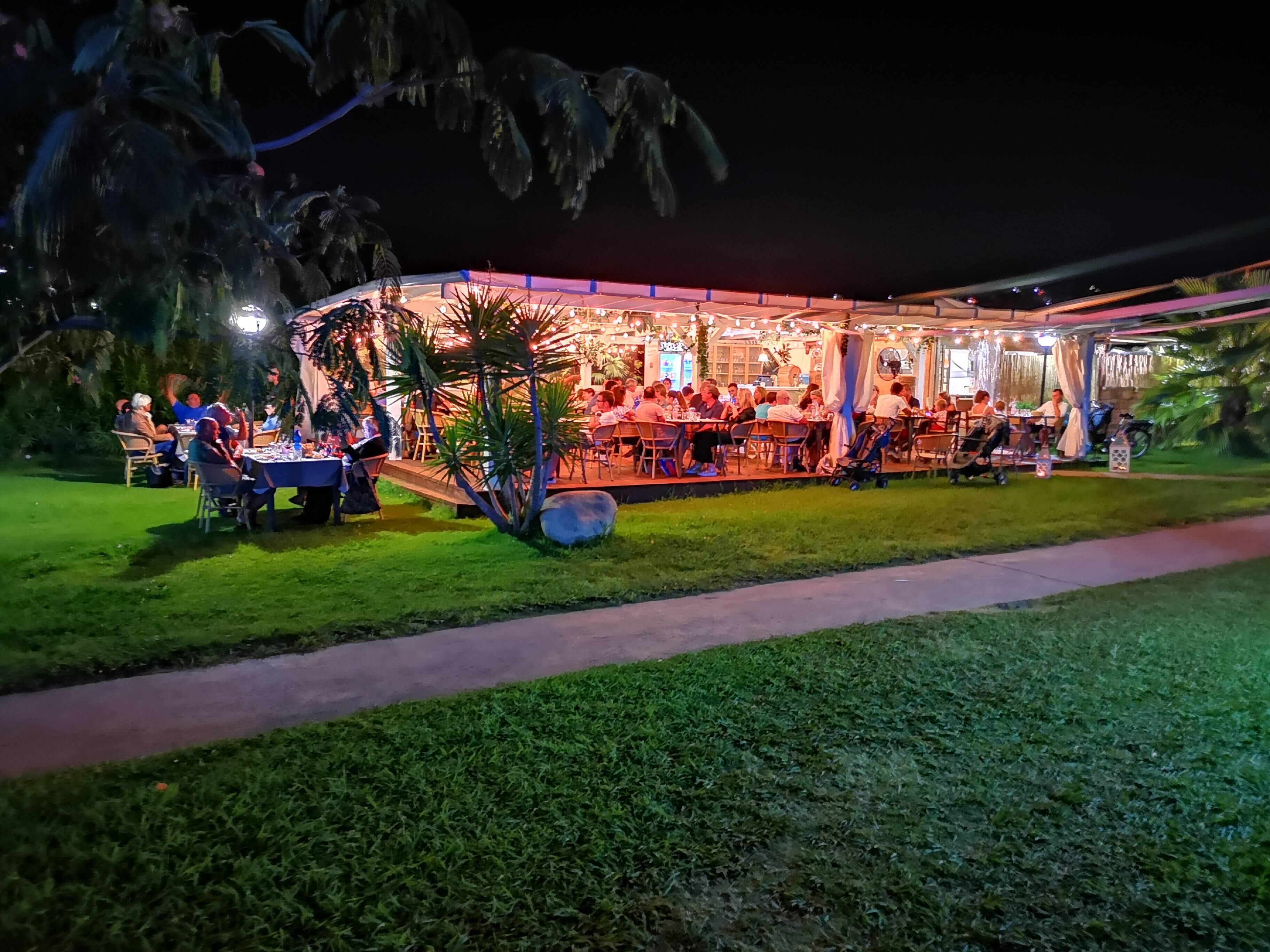 An outdoor restaurant with tables and chairs, surrounded by greenery.