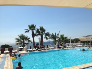 A swimming pool with lounge chairs and palm trees, surrounded by a clear view of the sea and distant mountains. - Sun and Sea Beach Hotel (Bodrum)