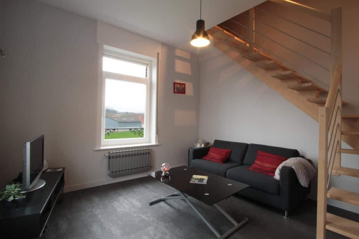 Ett modernt vardagsrum med en svart soffa, ett soffbord, en tv och ett fönster med utsikt över ett grönskande landskap.