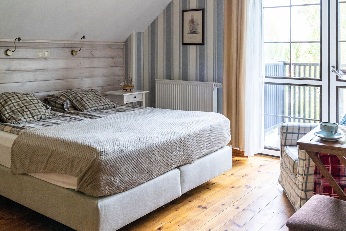 A bedroom with a bed, a bedside table, a radiator, a window with a view of the outdoors, and a small table with a cup.