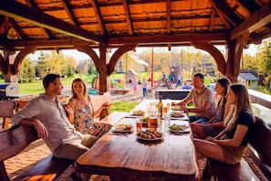 Ein hölzernes Pavillon mit einem für eine Mahlzeit gedecktem Tisch, umgeben von Menschen.