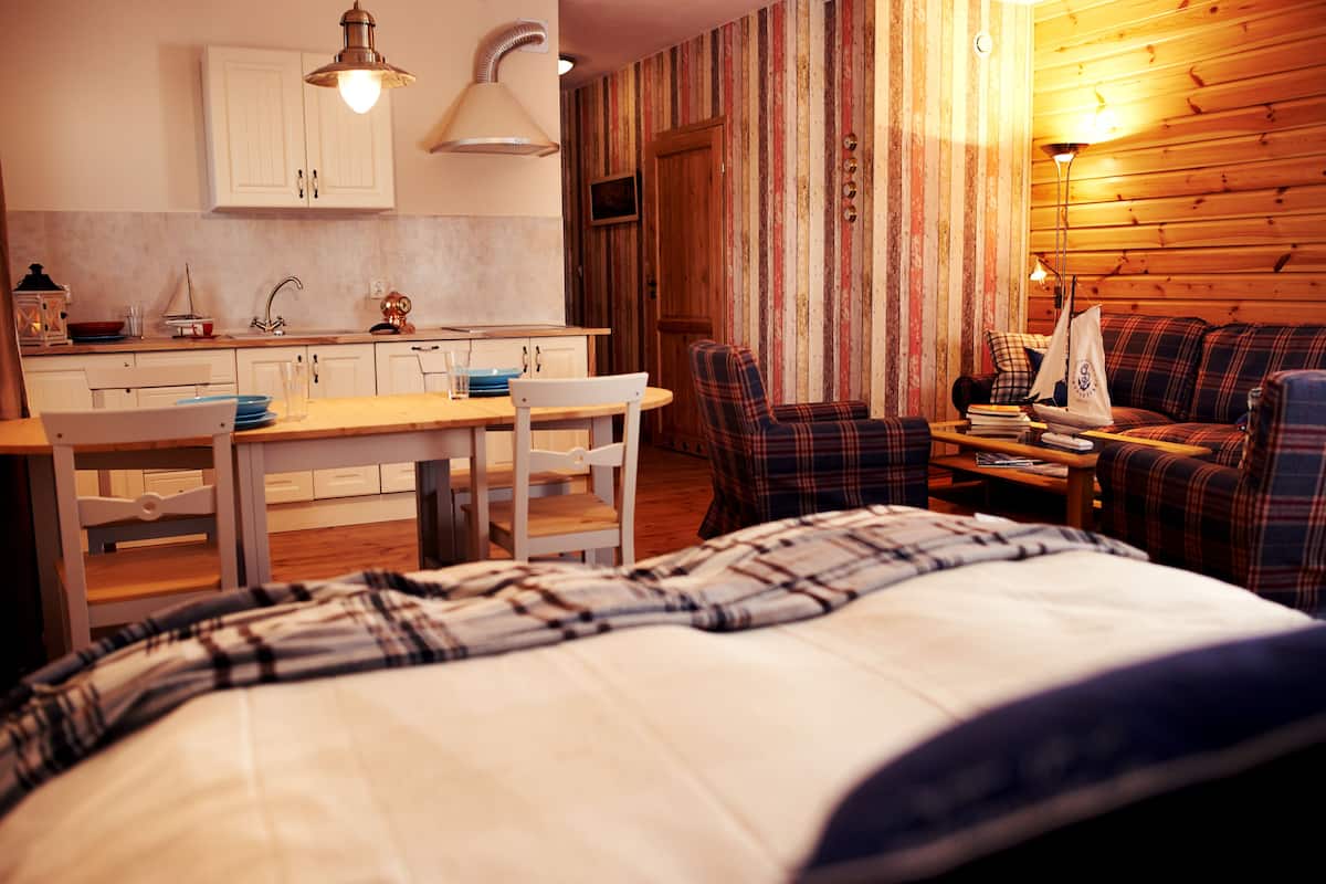 A cozy room with a bed, a dining table with chairs, a sofa, and a kitchen area with cabinets and a sink.