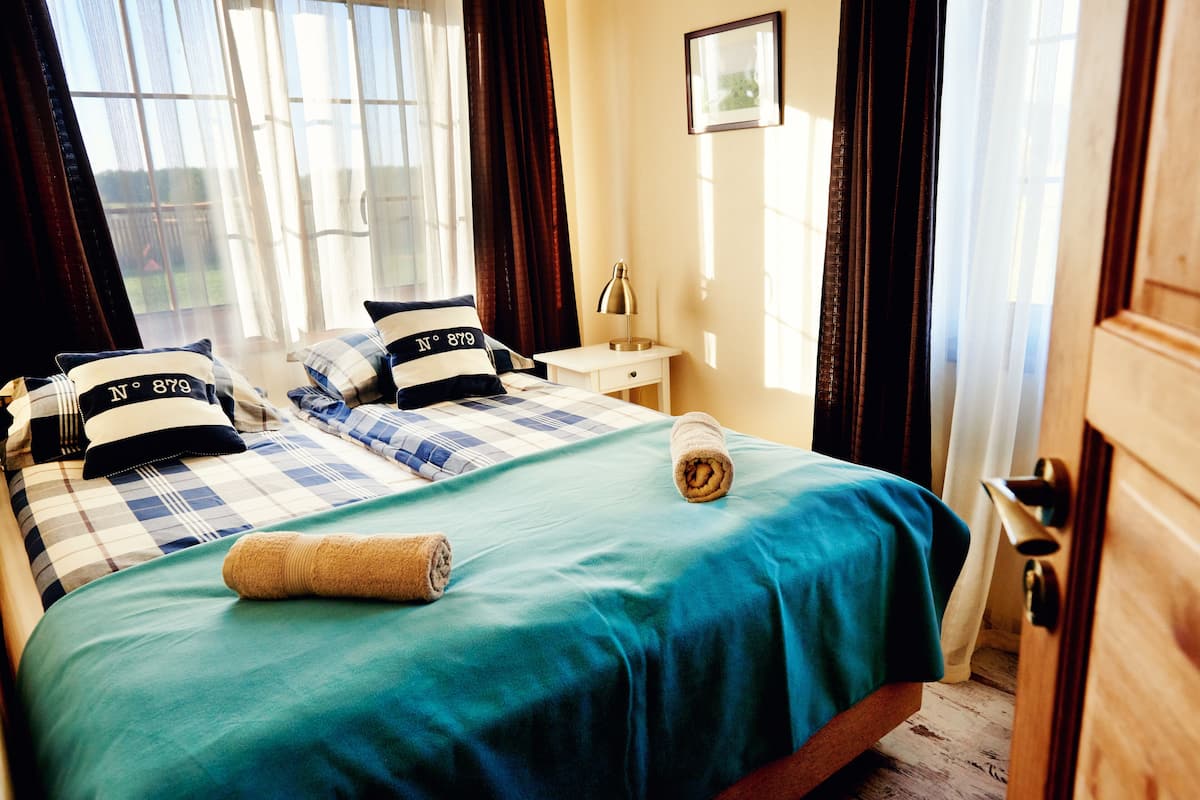 A hotel room with a bed, a nightstand, a lamp, and a window with curtains.