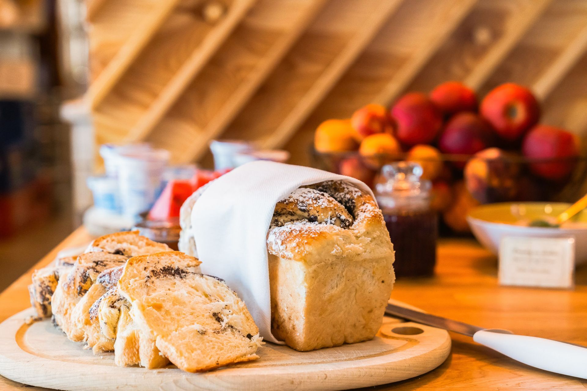 A loaf of bread with a dusting of powdered sugar, sliced pieces on a wooden board, and a knife.