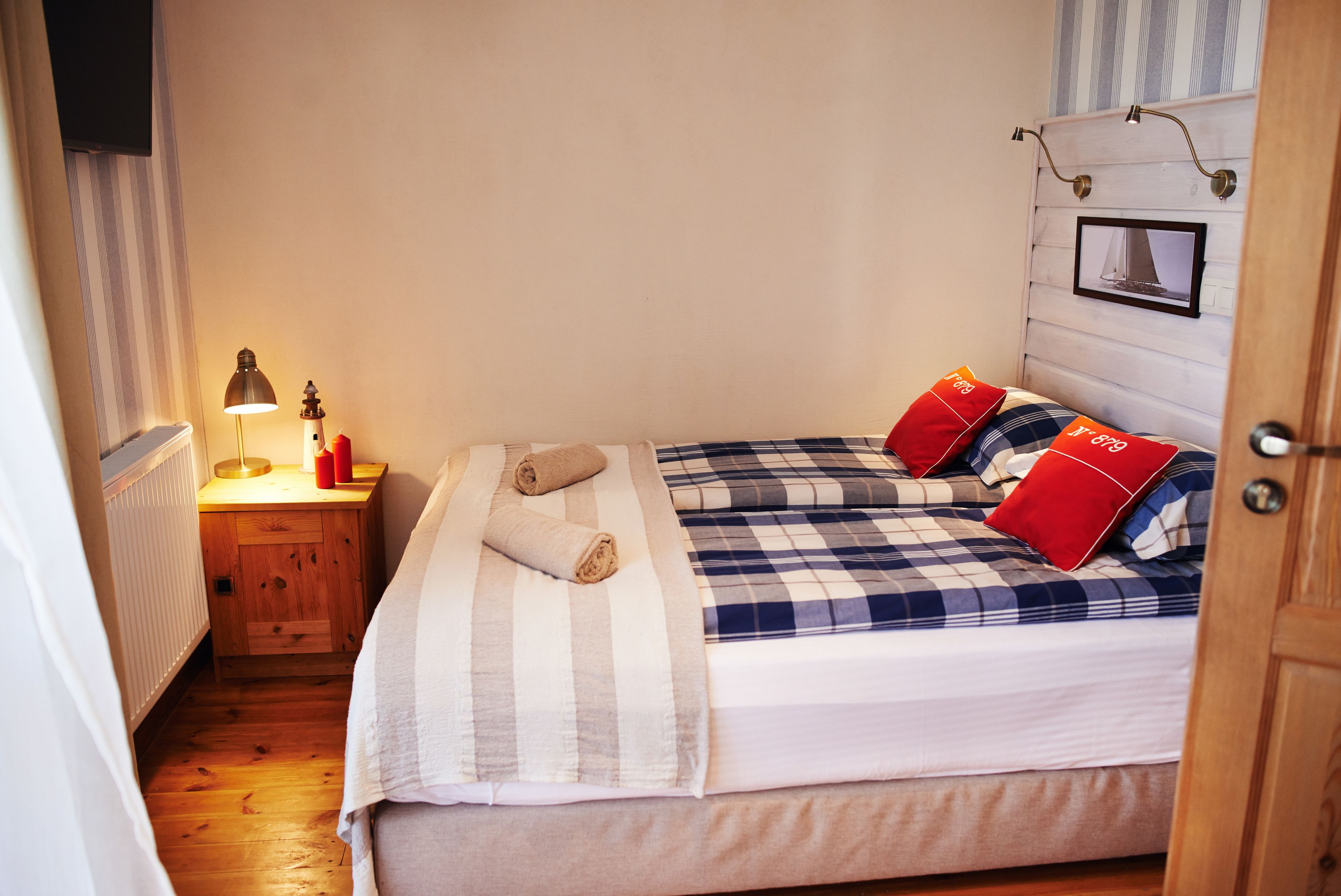 A neatly made bed with striped bedding, a bedside table with a lamp, and a framed picture on the headboard.