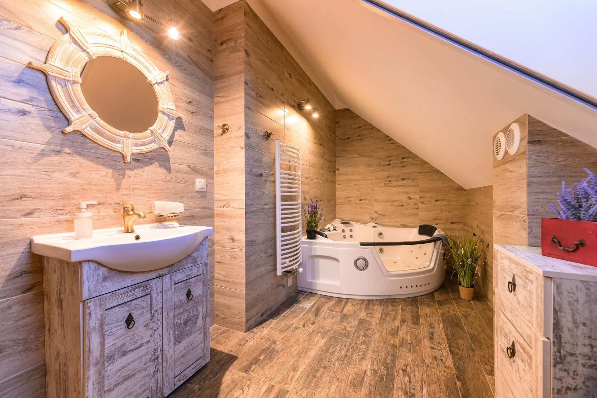 A modern bathroom with a wooden vanity, a freestanding bathtub, and a round mirror.