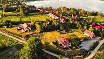 An aerial view of a lakeside village with traditional houses, a swimming pool, and a large barn.