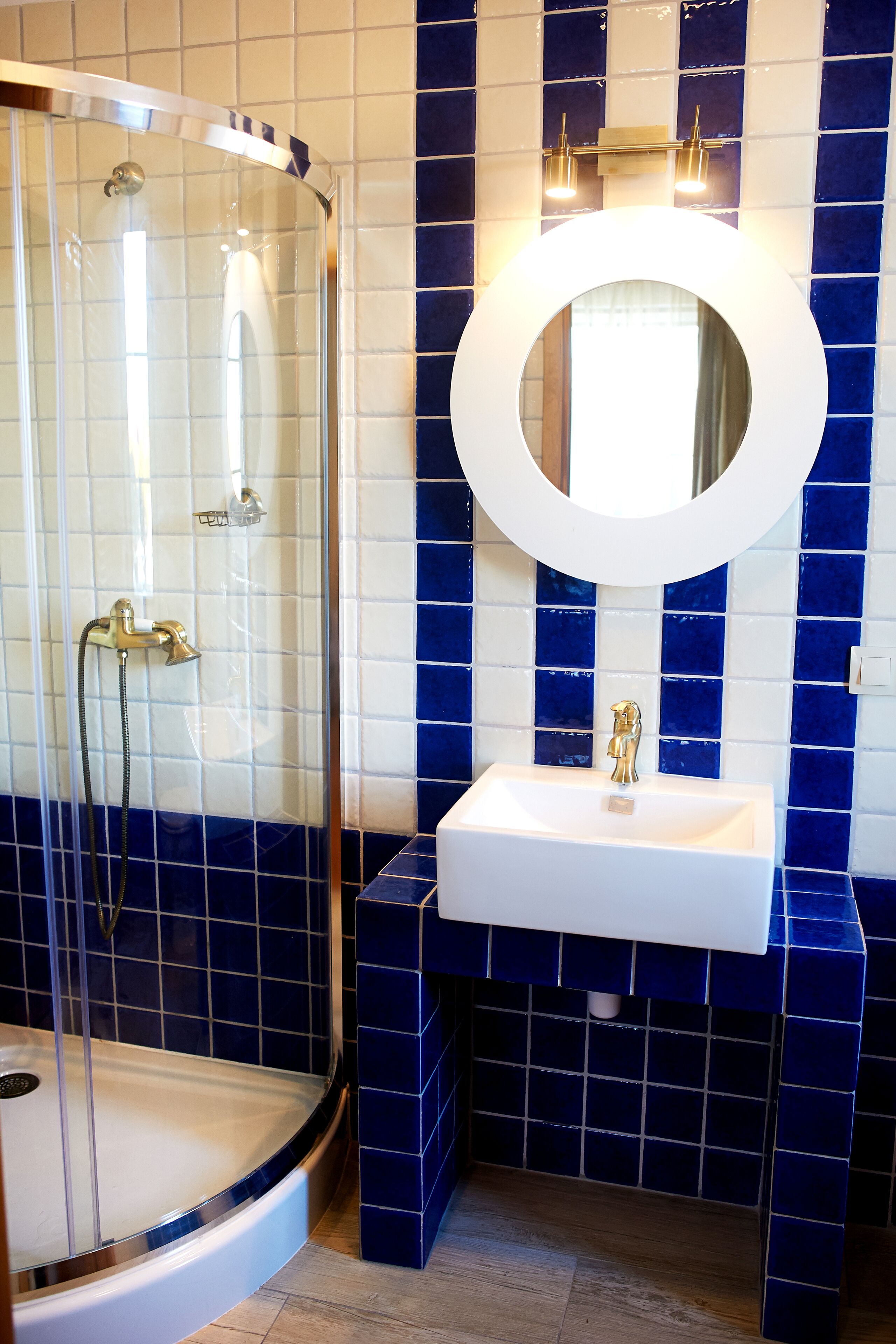 A bathroom with a glass-enclosed shower, a white sink with a gold faucet, and a large mirror above the sink.