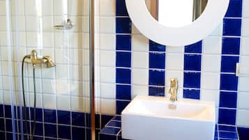 A bathroom with a glass-enclosed shower, a white sink with a gold faucet, and a large mirror above the sink.