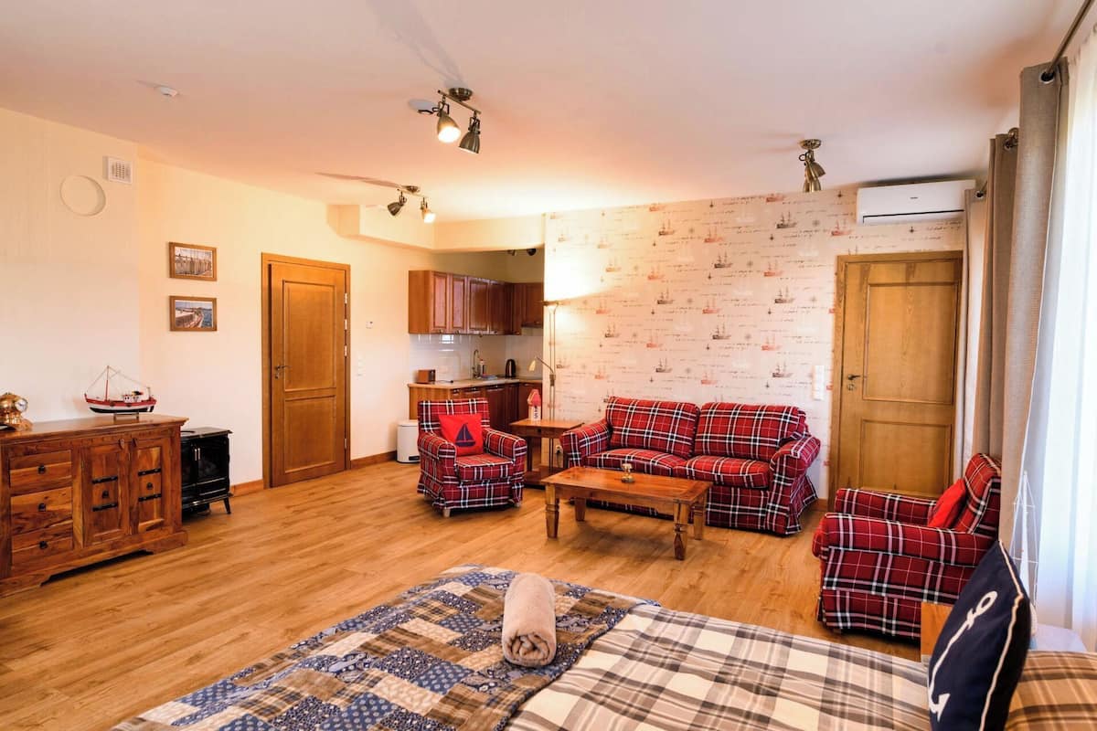 A cozy room with a bed, a red plaid sofa, a wooden cabinet, and a kitchen area.