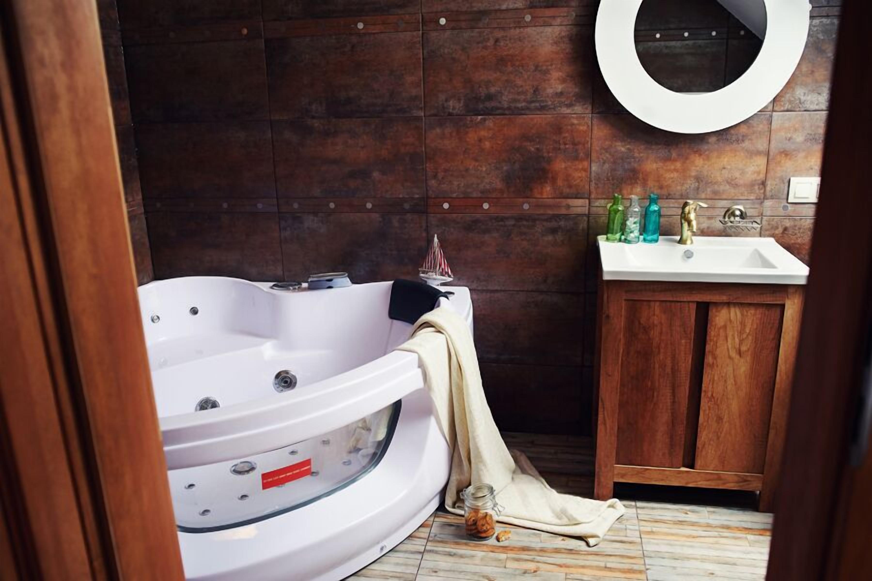 Un baño con una bañera blanca, un tocador de madera y un espejo redondo.