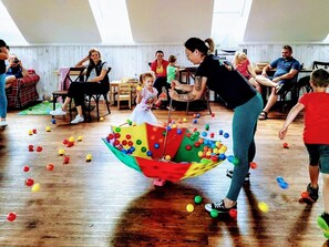 Ein Zimmer mit Holzboden, einer Personengruppe und einem bunten Spielbereich mit Bällen.